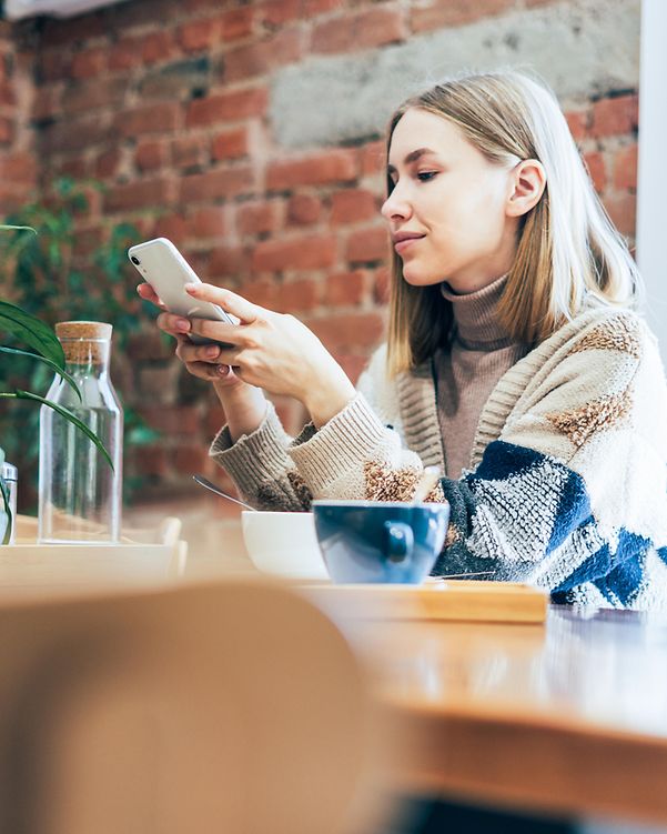 Junge Frau nutzt über das Smartphone Microsoft 365 beim Sitzen am Tisch