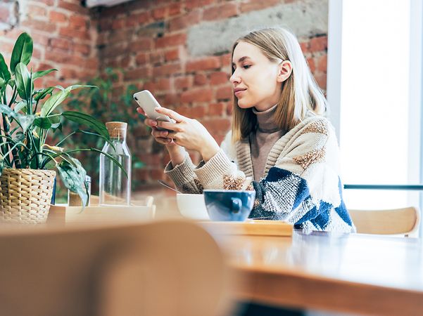 Eine Geschäftsfrau in einem Cafe informiert sich auf dem Handy via Business VPN über die Arbeit