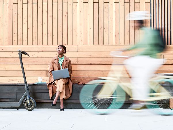Eine Geschäftsfrau sitzt vor einer holzverkleideten Mauer, und arbeitet mobil via Business VPN