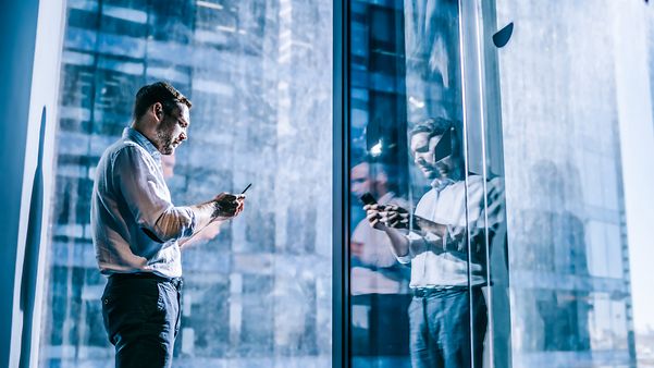 Mann, vor dem Fenster stehend, mit Smartphone in der Hand, das von Samsung Knox geschützt wird