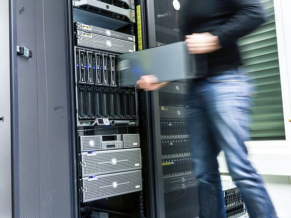 Ein IT Engineer steht mit Laptop vor einem geöffnetem Serverschrank und prüft die Interaktion mit Azure Cloud