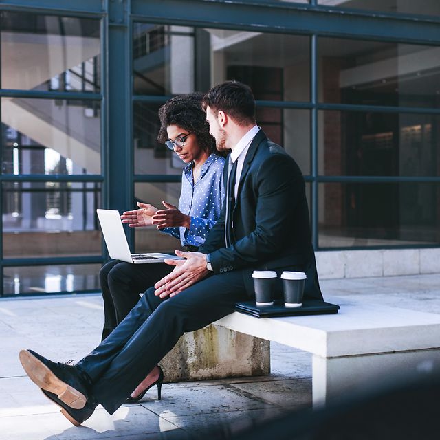 Zwei Kollegen sitzen auf einer Bank außerhalb eines Gebäudes und arbeiten über Azure Virtual Desktop