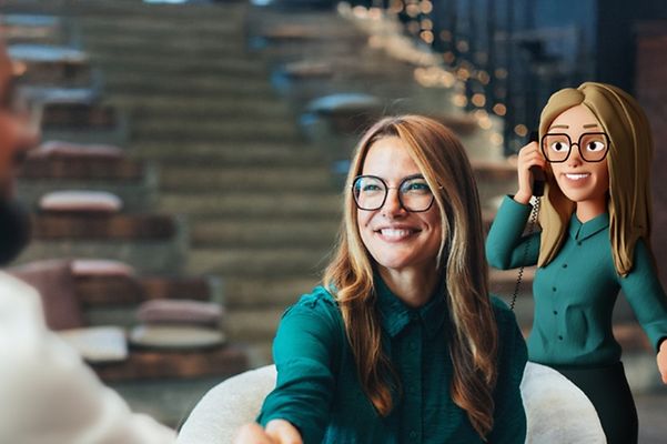 Junge Frau reicht Gesprächspartner die Hand während der Voice Bot im Hintergrund ein Telefonat annimmt.