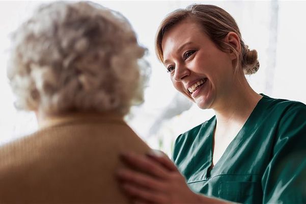 Pflegerin legt lächelnd einer älteren Frau eine Hand auf den Rücken