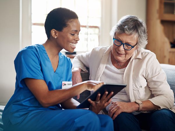 Lächelnde Pflegerin der AWO Schwaben schaut mit aelterer Dame auf ein iPad
