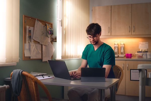 Pfleger dokumentiert seine Arbeit im Dienstzimmer am Laptop