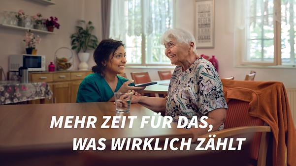 Pflegerin und ältere Dame verständigen sich über eine Übersetzungs-App auf dem Smartphone