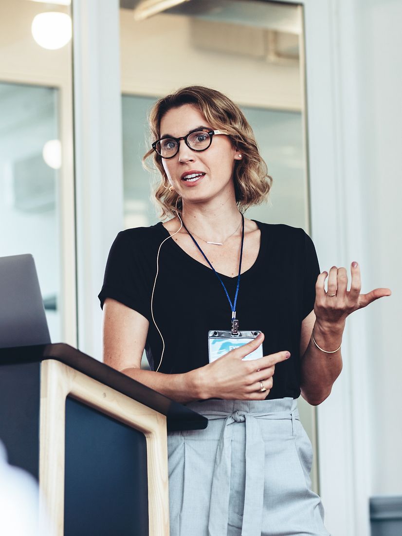 Zwei Personen, eine Frau und ein Mann, sprechen miteinander an einem Schreibtisch mit vielen Monitoren