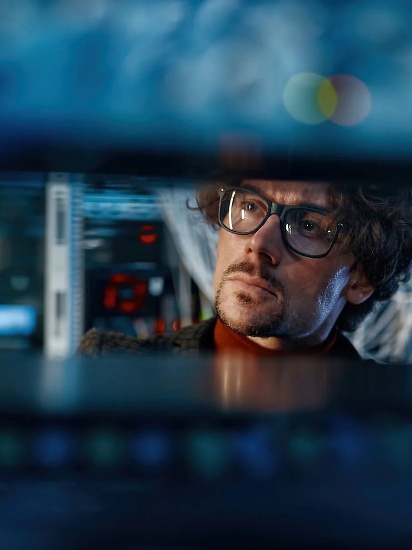 Zwei Personen, eine Frau und ein Mann, sprechen miteinander an einem Schreibtisch mit vielen Monitoren