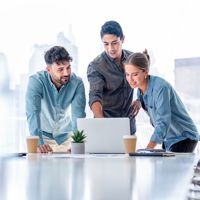 Drei Personen schauen auf einen Laptop-Bildschirm und besprechen ein Projekt.